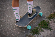 Lifestyle shot of purple crew socks with a turtle pattern, worn with sneakers and a skateboard.